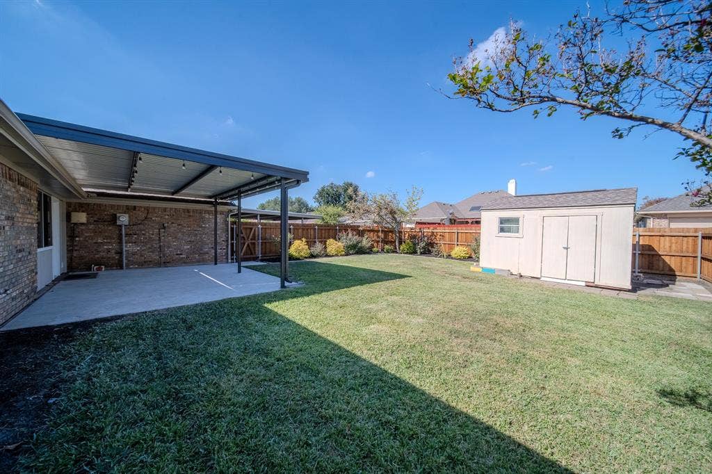 2213 Moore Drive, Plano, TX 75074 Backyard featuring a covered concrete patio, detached storage shed, privacy wood fencing, and open lawn space