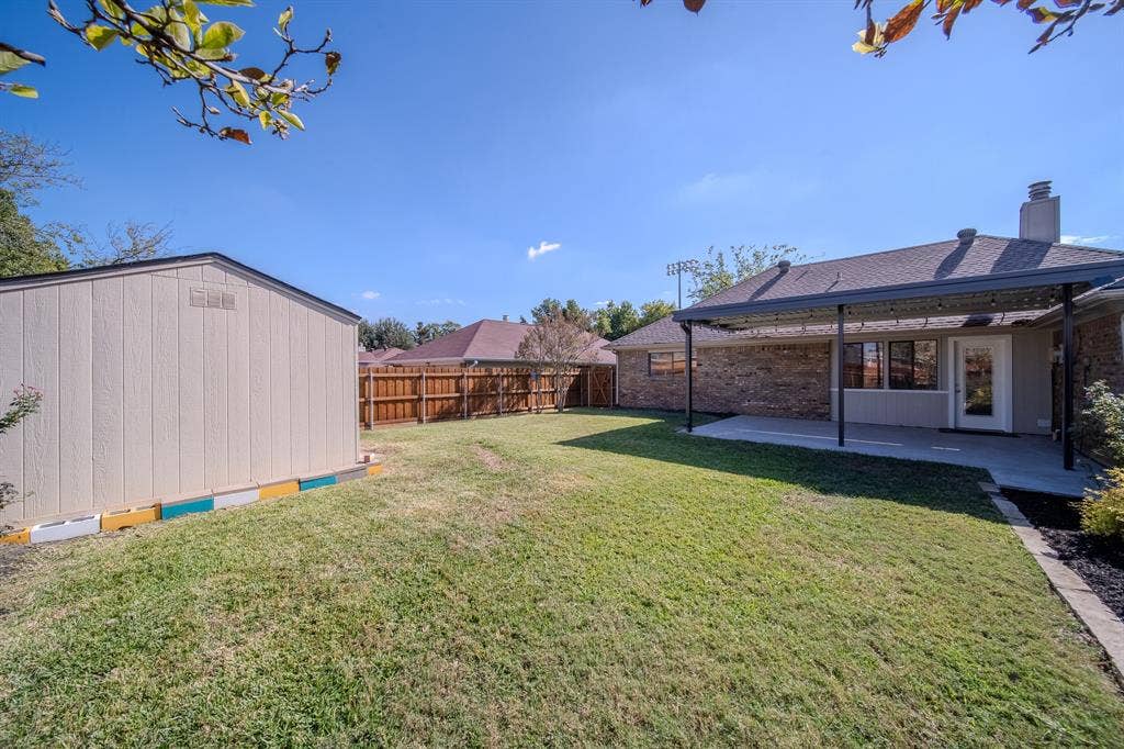 2213 Moore Drive, Plano, TX 75074 Rear exterior featuring a covered patio, brick masonry siding, a detached storage structure, and a fenced backyard