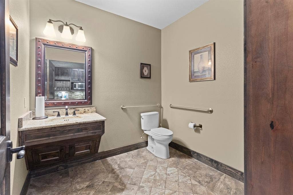 700 N Main Street, Lindale, TX 75771 Custom wooden vanity with stone countertop, decorative metal-trimmed mirror, three-light fixture, and stone-tile flooring