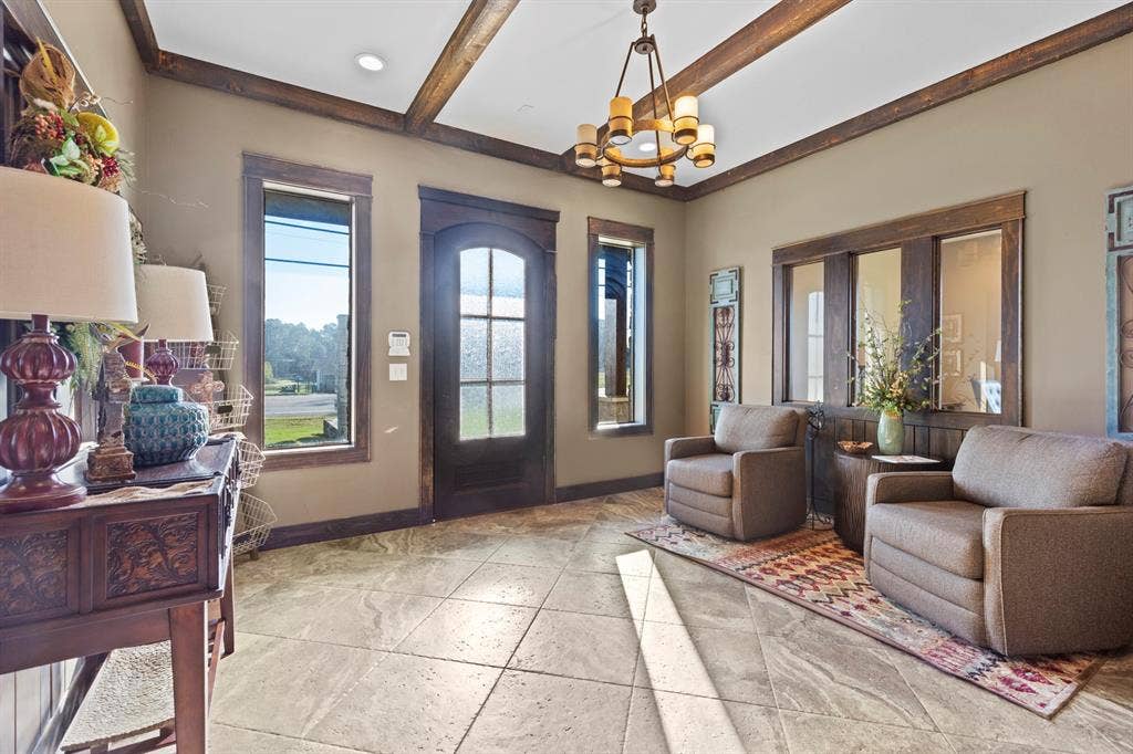 700 N Main Street, Lindale, TX 75771 Entryway featuring stone-tile flooring, wood-framed windows, a decorative wood-paneled door, exposed ceiling beams, and a tiered chandelier