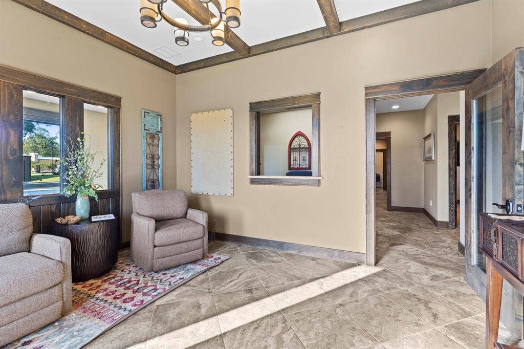 700 N Main Street, Lindale, TX 75771 Interior space featuring stone tile flooring, exposed wood ceiling beams, rustic wood trim detailing, a pass-through window with a stone sill, and a multi-arm chandelier