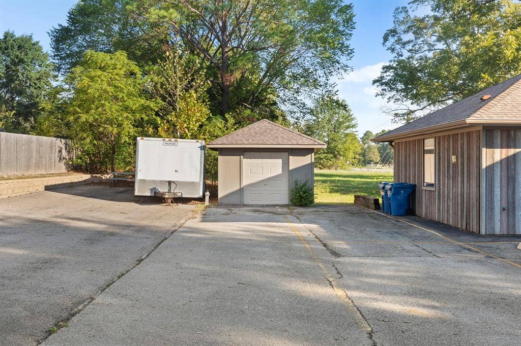 700 N Main Street, Lindale, TX 75771 Concrete driveway leading to a detached single-car garage with a hipped roof, vertical wood siding, and mature trees