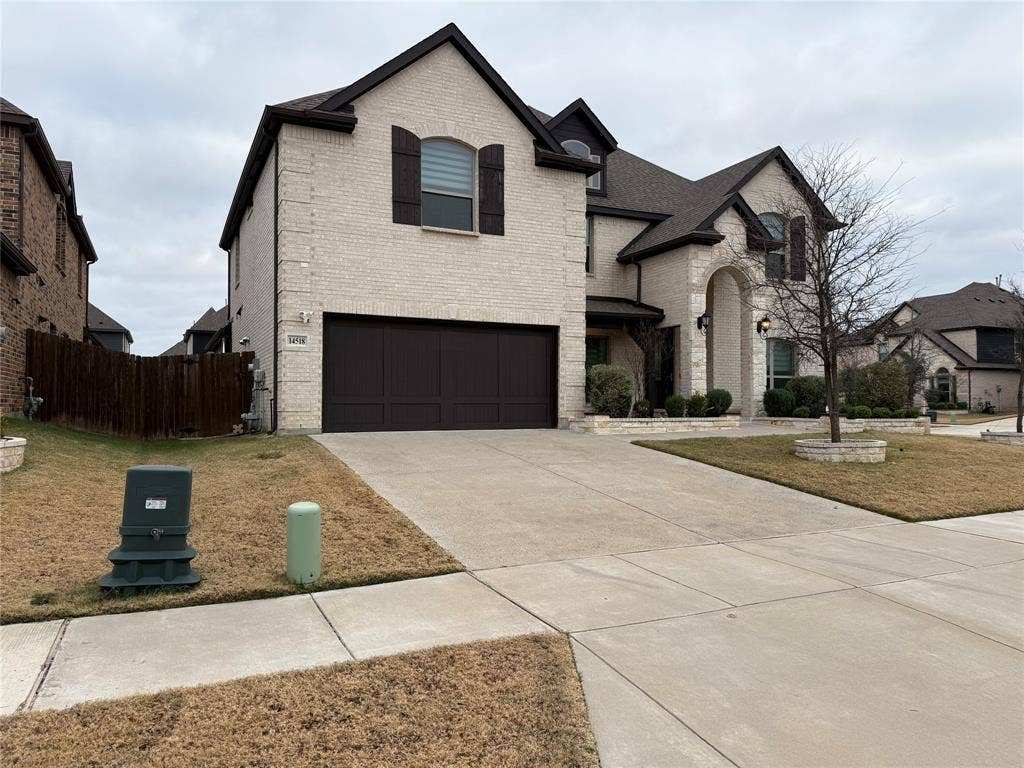 14518 Shady Grove Lane, Frisco, TX 75035 Two-story exterior featuring light-toned masonry, an arched stone-trimmed entryway, dark-finish shutters, and a multi-car garage