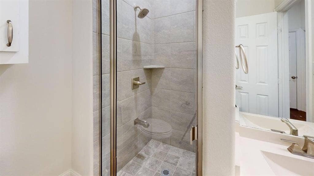 14518 Shady Grove Lane, Frisco, TX 75035 Walk-in shower enclosure with neutral-toned tiled walls, built-in corner shelf, and metallic fixtures, featuring a vanity with a solid surface countertop and undermount basin