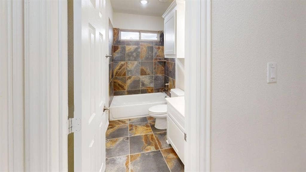 14518 Shady Grove Lane, Frisco, TX 75035 Bathroom featuring multi-tonal stone tile flooring and shower surround, white cabinetry, and a transom window
