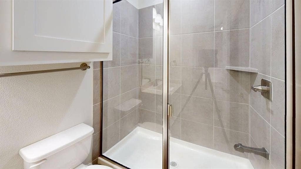 14518 Shady Grove Lane, Frisco, TX 75035 Walk-in shower featuring large-format ceramic tile surround, integrated shelving, glass enclosure with metallic trim, and wall-mounted shower fixture