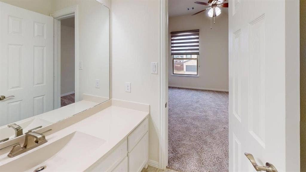 14518 Shady Grove Lane, Frisco, TX 75035 Bathroom featuring a white vanity with integrated sink, polished metal faucet, large frameless mirror, and neutral wall-to-wall carpeting