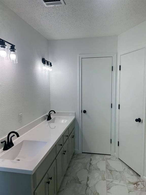 1114 Idlewood Drive, Waco, TX 76705 Dual-vanity cabinet featuring a white solid-surface countertop with integrated sinks, matte black widespread faucets, matching matte black vanity lighting, and light-toned tile flooring