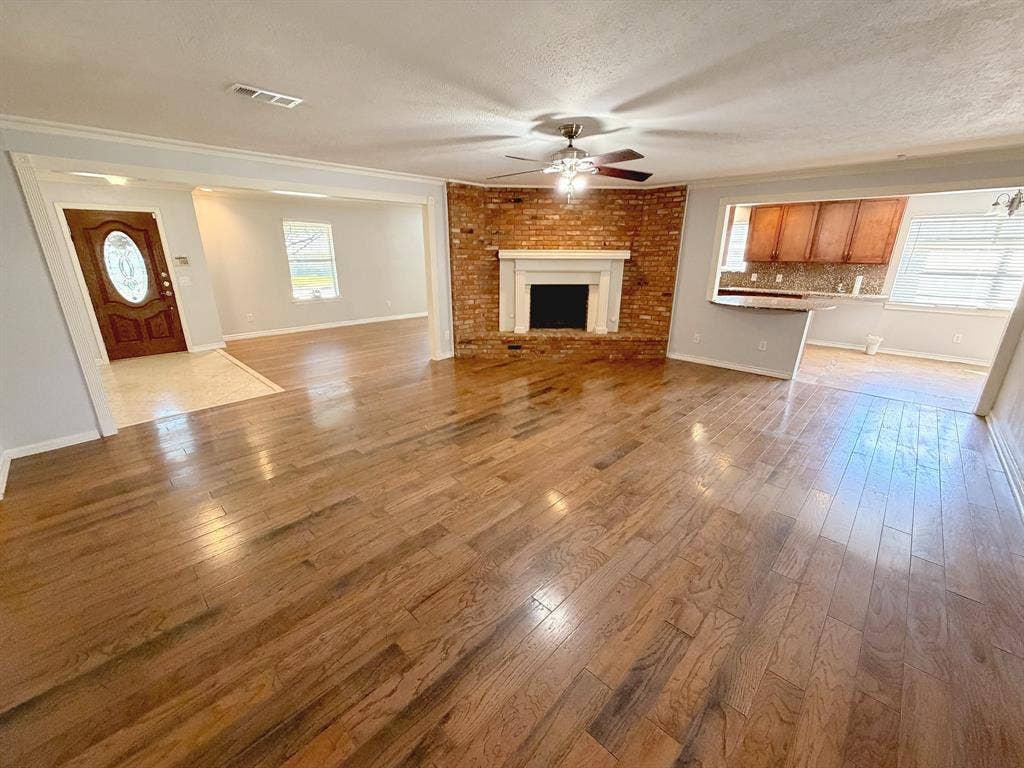 2701 Northcrest Drive, Plano, TX 75075 Corner brick fireplace with a white mantel, wood-finish flooring, and ceiling fan with integrated lighting