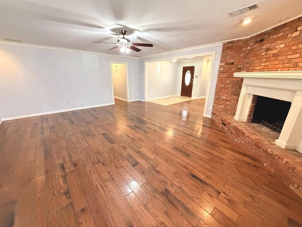 2701 Northcrest Drive, Plano, TX 75075 Living area featuring wood-finish flooring, a floor-to-ceiling brick fireplace with a decorative mantel, and a ceiling fan with integrated lighting