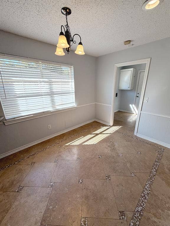 2701 Northcrest Drive, Plano, TX 75075 Interior space featuring large-format tile flooring with decorative stone-accented borders, white wainscoting, a three-light chandelier, and horizontal window blinds