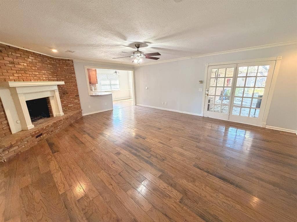 2701 Northcrest Drive, Plano, TX 75075 Living area featuring wood-finish flooring, a red brick fireplace with a white mantel, and glass-paned French doors