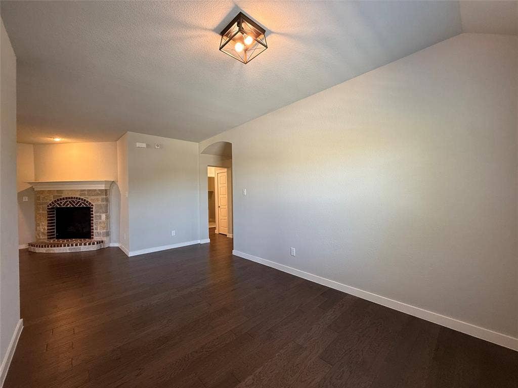 1702 Sagebrush Trail, Wylie, TX 75098 Living area featuring wood-finish flooring, vaulted ceilings, a geometric metal-frame light fixture, and a stone-surround corner fireplace with brick detailing