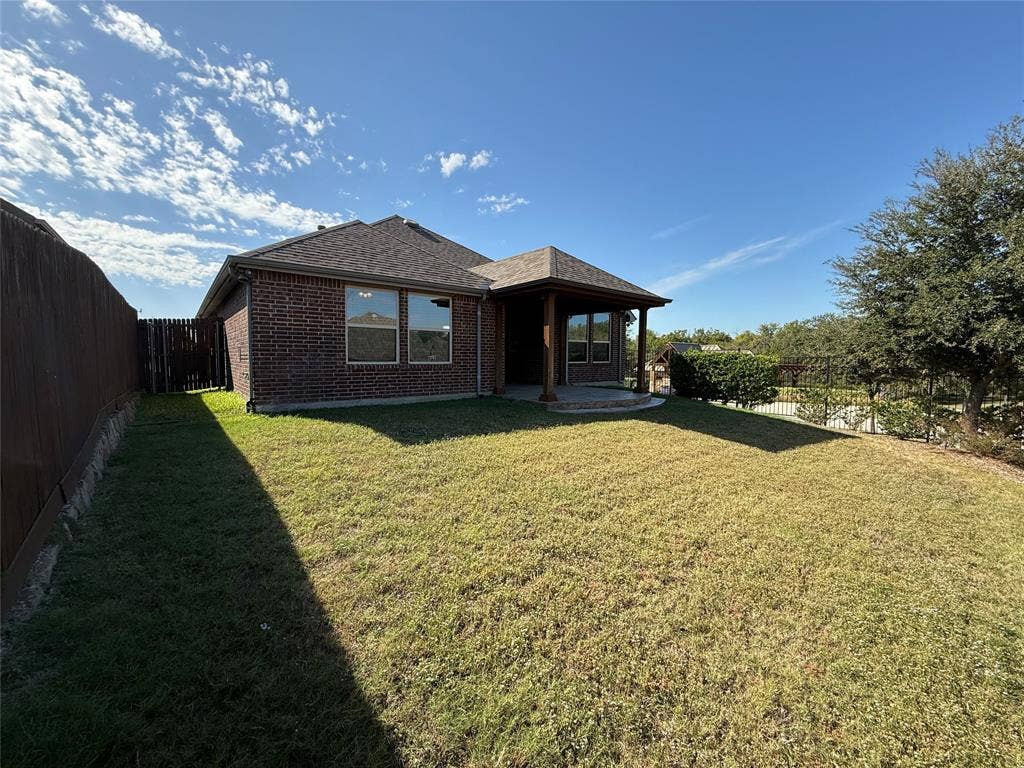 1702 Sagebrush Trail, Wylie, TX 75098 Brick exterior with a covered rear patio, shingled hip roof, and wood fencing