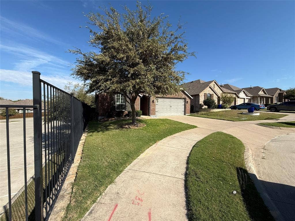 1702 Sagebrush Trail, Wylie, TX 75098 Brick exterior with attached two-car garage, metal picket fencing, and mature landscaping