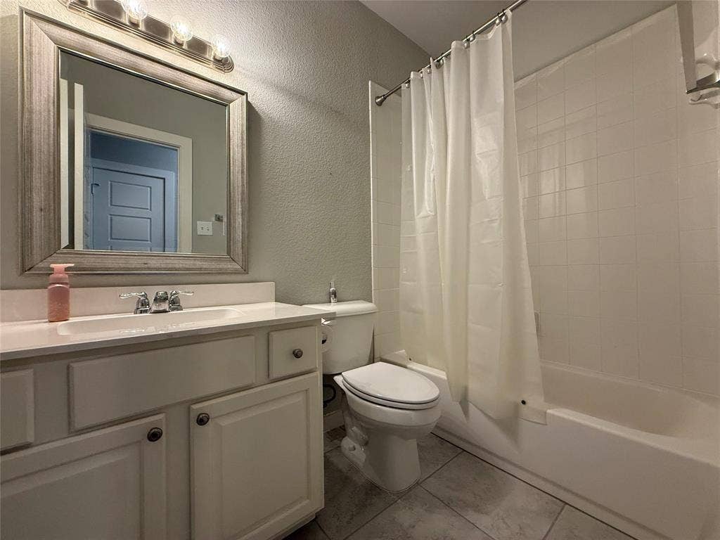 1702 Sagebrush Trail, Wylie, TX 75098 Bathroom featuring a white vanity cabinet with an integrated countertop, framed wall mirror, multi-bulb overhead lighting, and a bathtub with tile surround