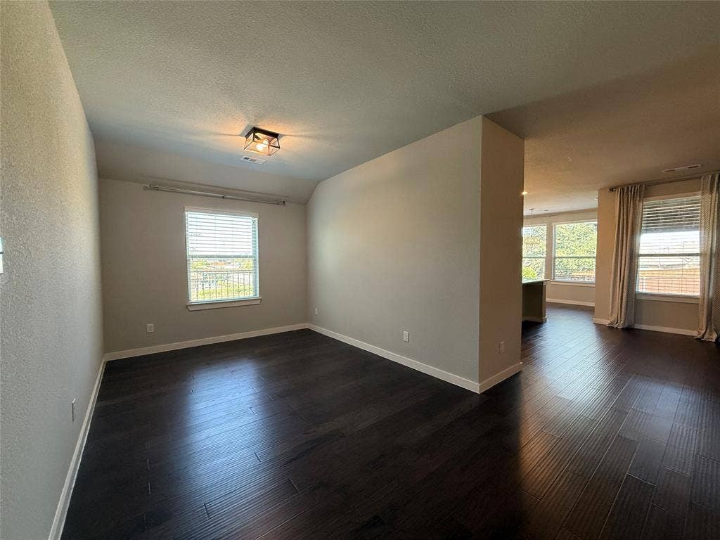 1702 Sagebrush Trail, Wylie, TX 75098 Spacious interior featuring dark wood-finish flooring, neutral wall paint, geometric flush-mount lighting, and large windows with horizontal blinds