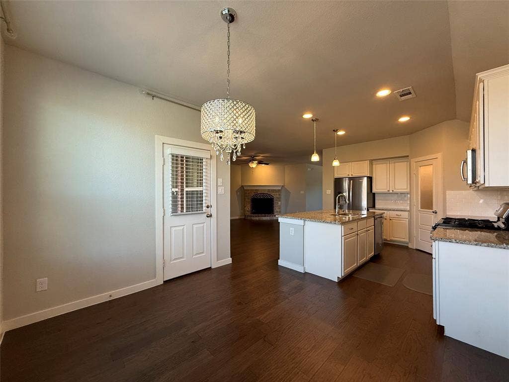 1702 Sagebrush Trail, Wylie, TX 75098 Kitchen featuring white cabinetry, stone countertops, stainless steel appliances, a center island with a built-in sink, and wood-finish flooring
