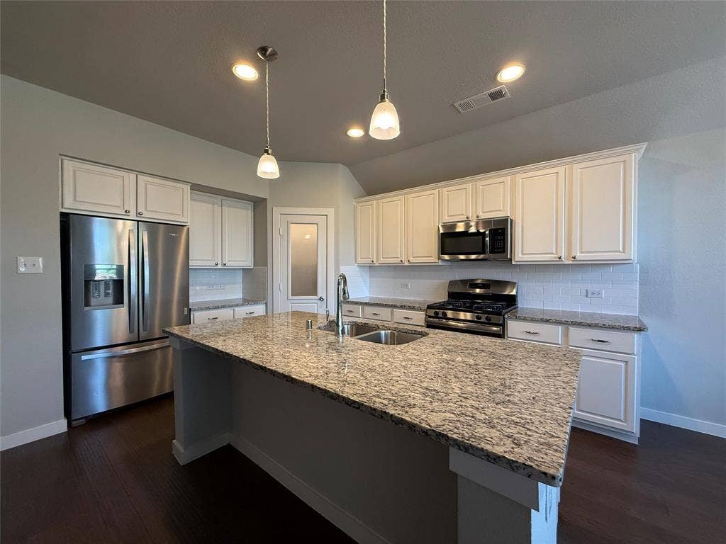 1702 Sagebrush Trail, Wylie, TX 75098 Kitchen featuring stone countertops, white cabinetry, stainless steel appliances, a central island with an integrated sink, and pendant lighting