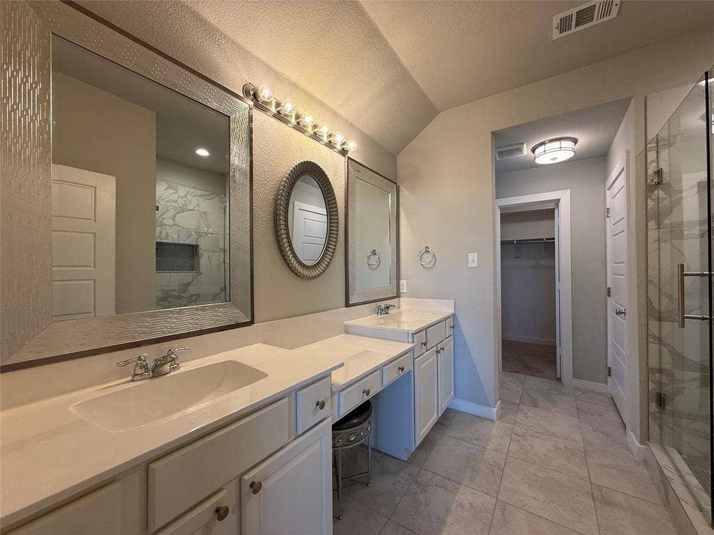 1702 Sagebrush Trail, Wylie, TX 75098 Dual-sink vanity with light-tone solid surface countertops, extensive wall-mounted mirrors, large-format tile flooring, and a glass-enclosed shower