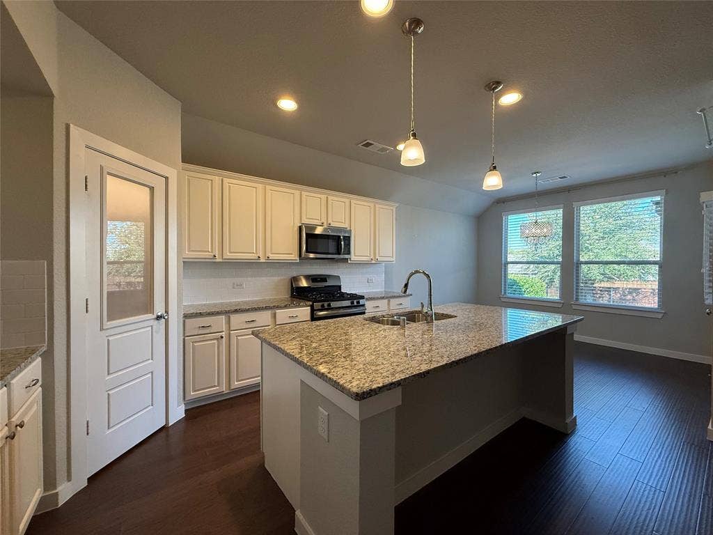 1702 Sagebrush Trail, Wylie, TX 75098 Kitchen featuring a central island with stone-finish countertops, shaker-style cabinetry, wood-finish flooring, glass-panel pantry door, and pendant lighting