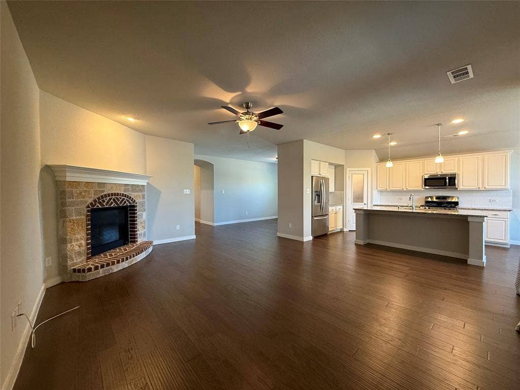 1702 Sagebrush Trail, Wylie, TX 75098 Open-concept interior featuring wood-finish flooring, a stone-surround fireplace with a brick-accented hearth, a kitchen island with stone countertops, and recessed lighting