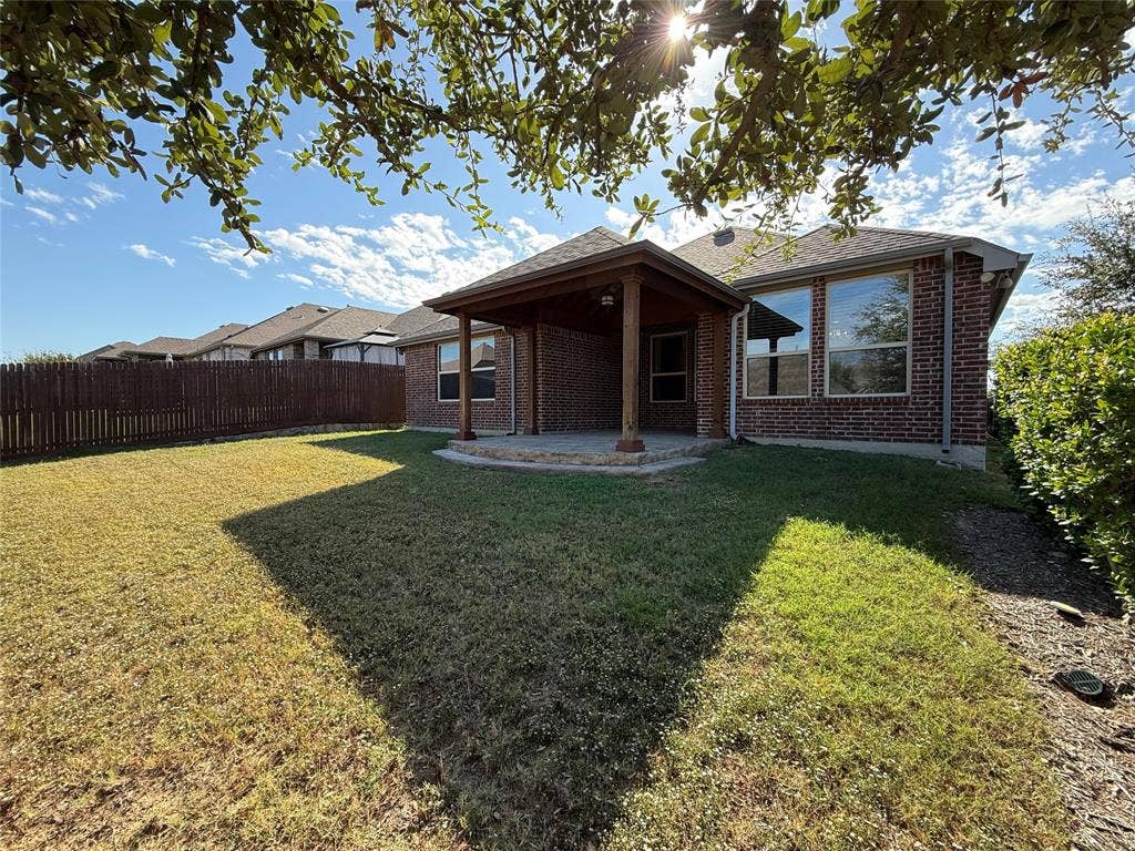 1702 Sagebrush Trail, Wylie, TX 75098 Brick exterior, covered rear patio with wood-column supports, and fenced backyard featuring a natural grass lawn