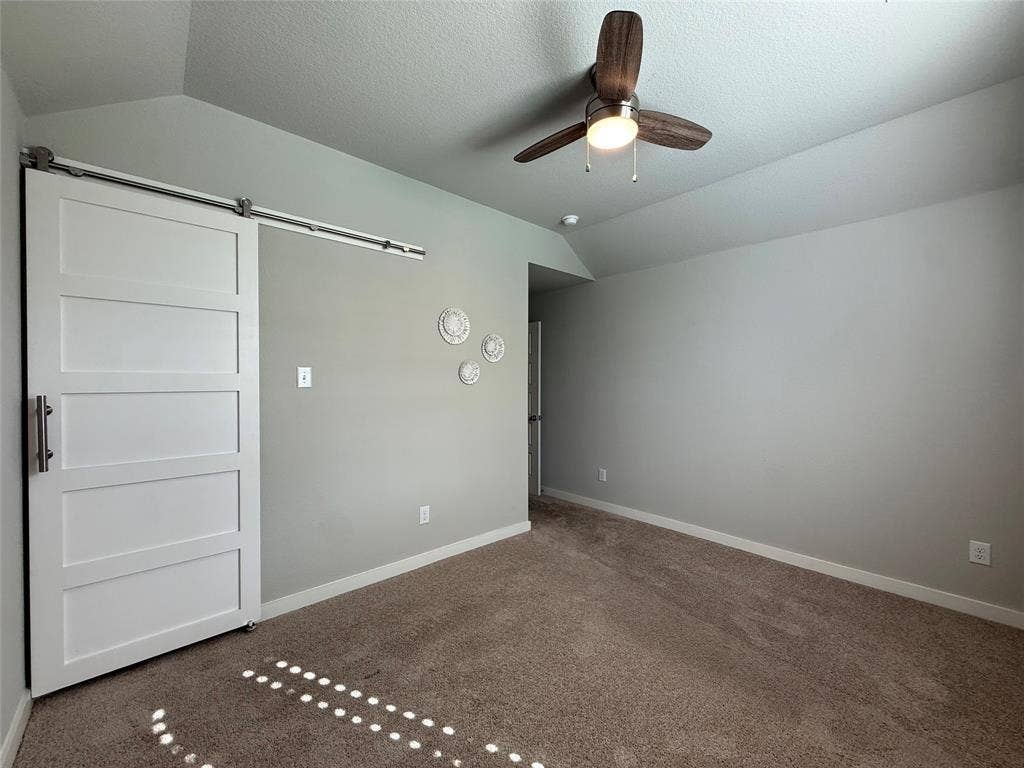1702 Sagebrush Trail, Wylie, TX 75098 Vaulted ceilings, carpeted flooring, and a white sliding barn door featuring a stainless steel track and hardware, complemented by a ceiling fan with integrated lighting