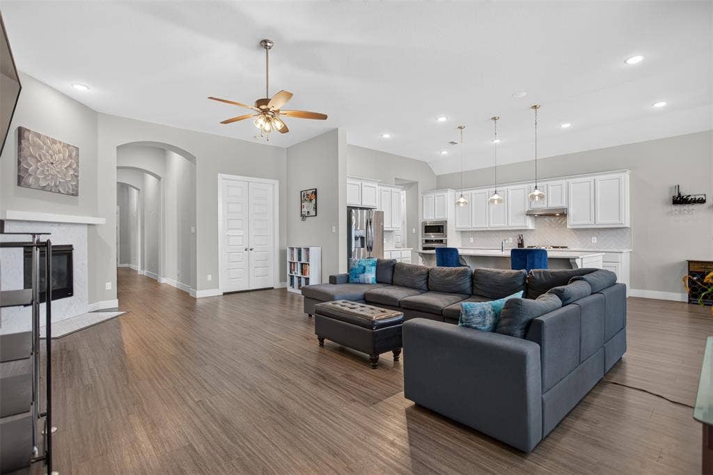 1103 Walford Drive, Forney, TX 75126 Open-concept living space featuring wood-finish flooring, high ceilings with recessed lighting, a stone-surround fireplace, and a kitchen equipped with white cabinetry and a central island with pendant lighting