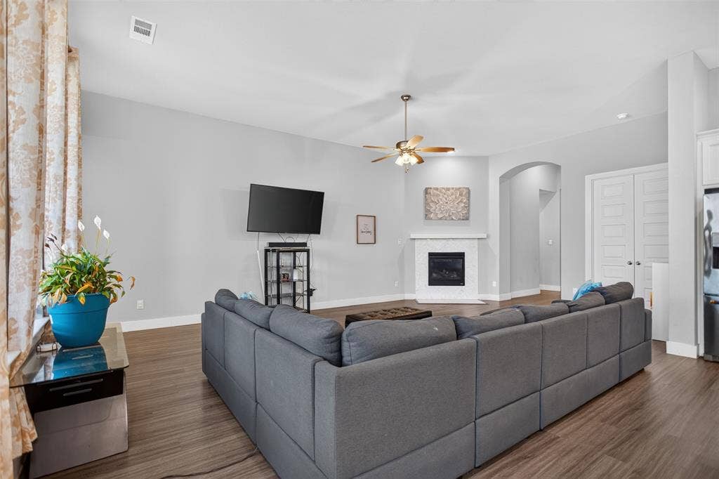 1103 Walford Drive, Forney, TX 75126 Living area featuring wood-finish flooring, vaulted ceilings, a fireplace with a white tile surround, a brushed metal ceiling fan, and arched architectural detailing