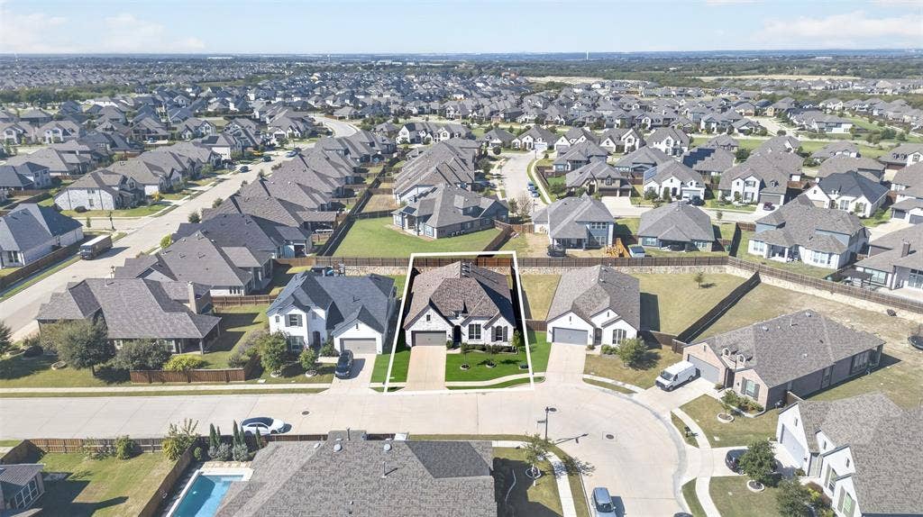 1103 Walford Drive, Forney, TX 75126 Aerial perspective featuring a multi-gabled roofline, brick and stone exterior, paved driveway, and perimeter wood fencing