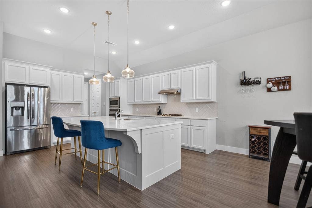 1103 Walford Drive, Forney, TX 75126 Kitchen featuring white cabinetry, an expansive island with a light-toned stone countertop, stainless steel refrigerator and built-in microwave, wood-finish flooring, and recessed lighting