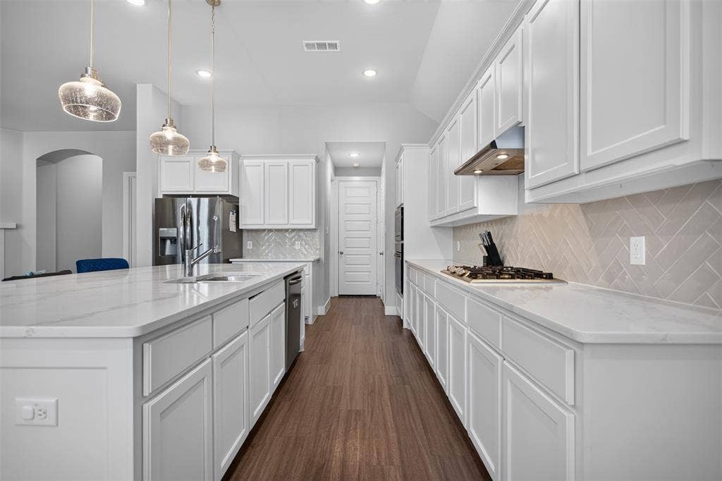 1103 Walford Drive, Forney, TX 75126 Kitchen featuring white shaker-style cabinetry, quartz countertops, a neutral herringbone-pattern backsplash, three glass pendant lights, and wood-finish flooring