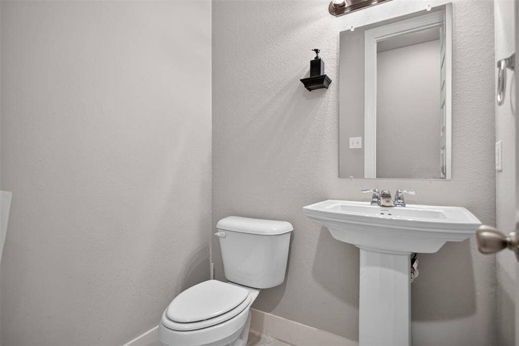 1103 Walford Drive, Forney, TX 75126 Bathroom featuring a white porcelain pedestal sink with a chrome dual-handle faucet, a wall-mounted rectangular mirror, and a wall-mounted light fixture
