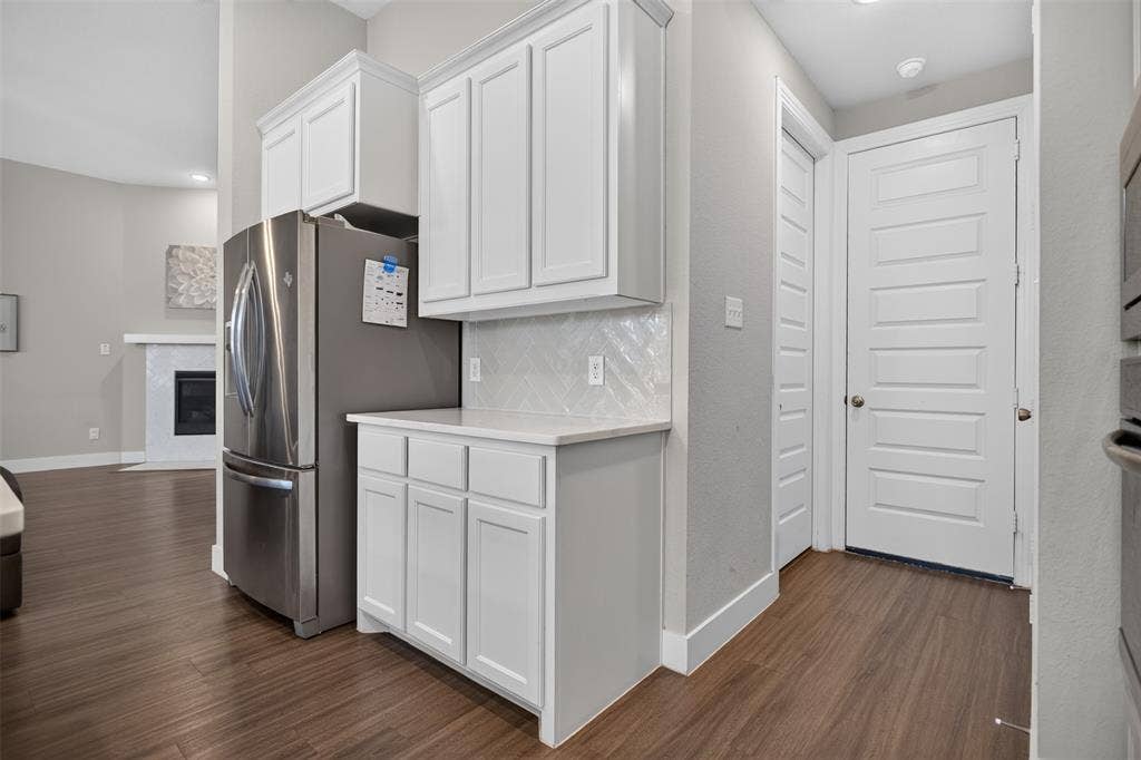 1103 Walford Drive, Forney, TX 75126 Kitchen area featuring white shaker-style cabinetry, herringbone-patterned tile backsplash, stone-surface countertop, stainless steel refrigerator, and wood-finish flooring
