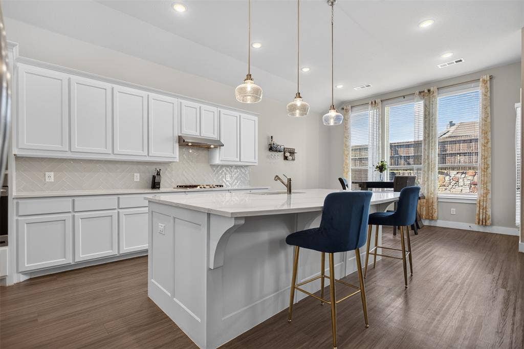 1103 Walford Drive, Forney, TX 75126 Kitchen featuring white shaker-style cabinetry, a central island with countertop seating, herringbone-patterned tile backsplash, pendant lighting, and wood-finish flooring