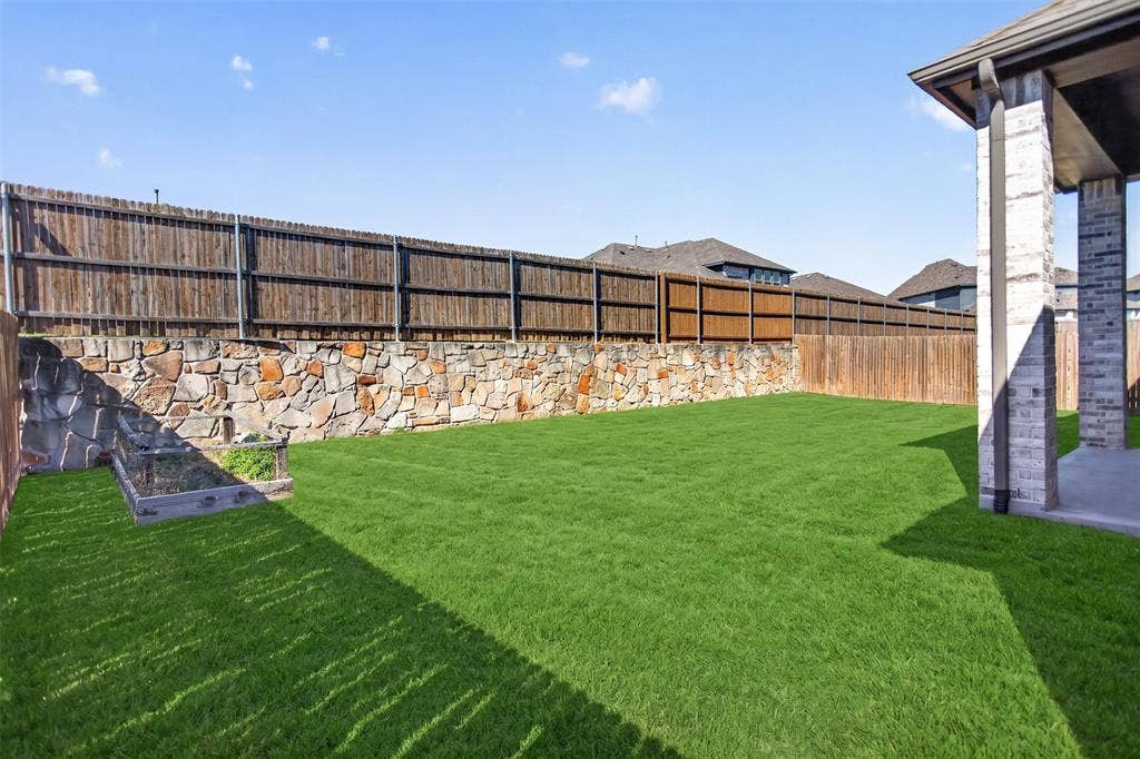 1103 Walford Drive, Forney, TX 75126 Backyard featuring a covered concrete patio, stone retaining wall, wood privacy fencing, and a built-in raised garden bed
