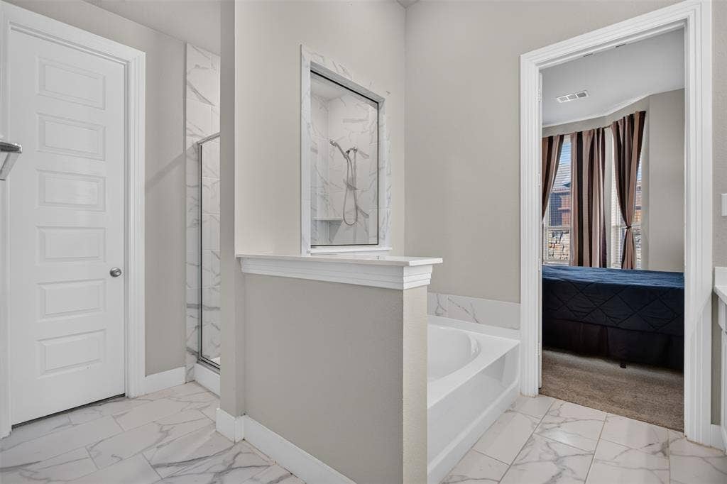 1103 Walford Drive, Forney, TX 75126 Bathroom featuring large-format tile flooring with marble-patterned finish, a built-in soaking tub, a separate shower enclosure with full-height tile surround, and a partial privacy wall