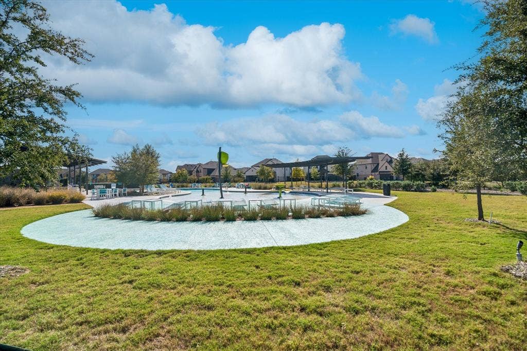 Community pool area featuring a tanning ledge, water feature, covered cabana structure, and expansive manicured lawn