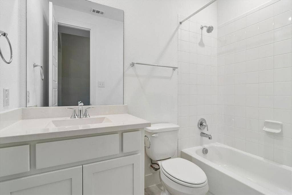 Bathroom featuring a white vanity with a composite countertop, an undermount sink, a full-width mirror, and a shower-tub combination with white wall tile