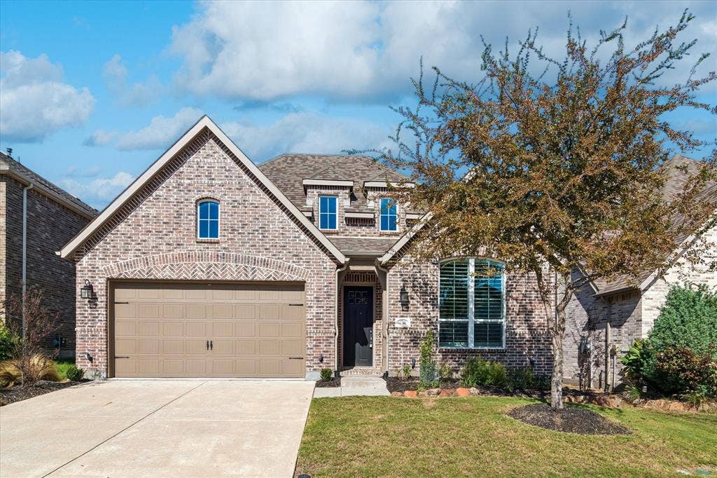 Brick exterior with arched detailing, multi-gabled roofline, concrete driveway, two-car garage, and arched window features