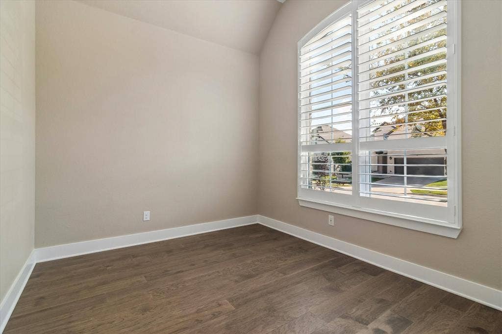 Room featuring a vaulted ceiling, wood-finish flooring, and a large arched window with integrated plantation shutters