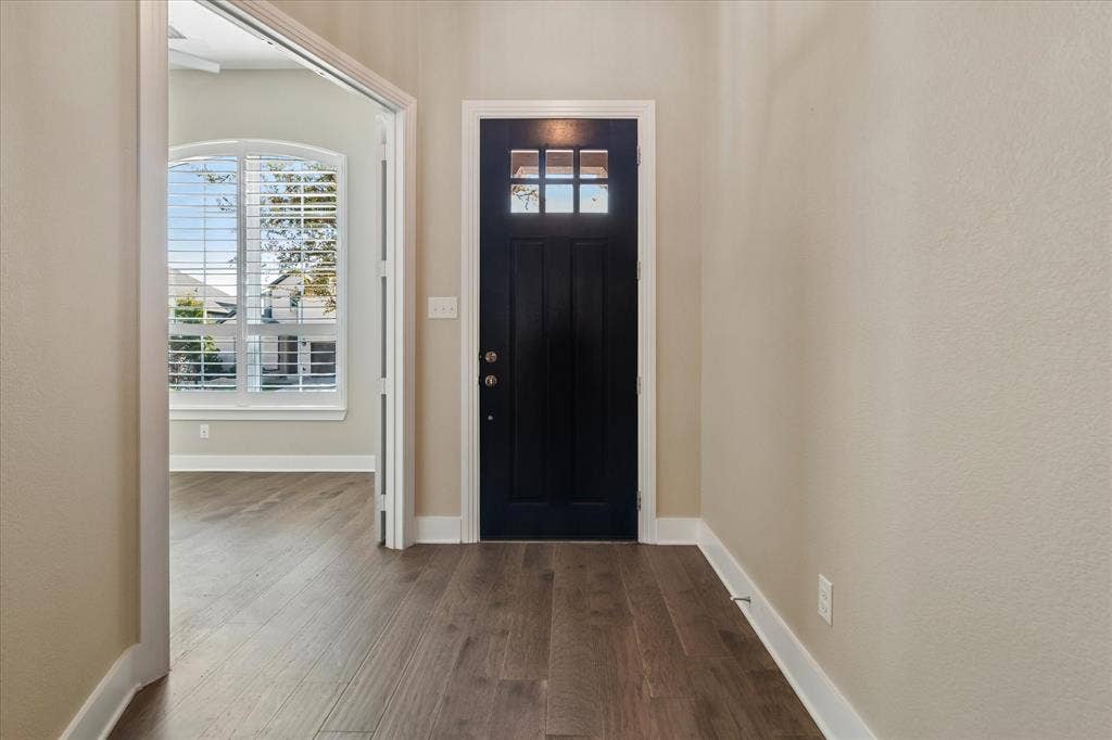 Entryway featuring a dark-toned door with a six-pane glass insert, wood-finish flooring, and arched window with plantation shutters