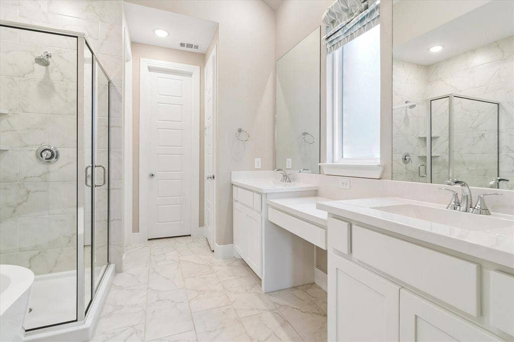Bathroom featuring a dual-sink vanity with a recessed center workspace, stone-finish tile flooring, walk-in shower with a glass enclosure, and wall-to-wall mirrors