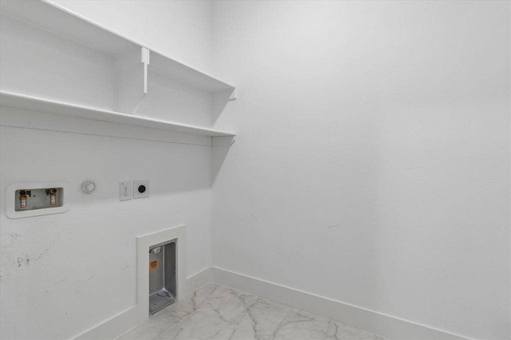 Utility space featuring white walls, built-in shelving, stone-finish tile flooring, and integrated laundry hookups