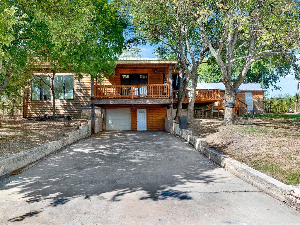 Log-style exterior with an elevated wooden deck, concrete driveway, attached garage, and stone-block retaining walls