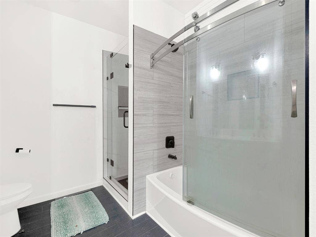 Bathroom featuring a separate glass-enclosed shower, a deep soaking tub with a sliding glass door, matte black fixtures, and wood-patterned tile surrounds