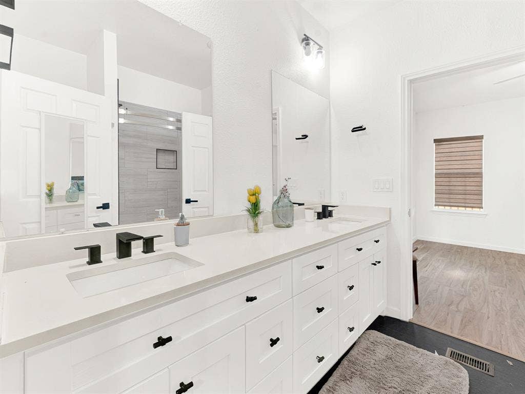 Dual-sink vanity with a solid-surface countertop, matte black fixtures, extensive cabinetry, and frameless wall-mounted mirrors
