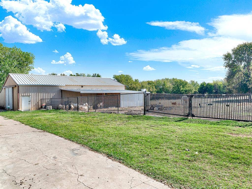 Metal-sided outbuilding featuring a pitched roof, attached metal awning, and fenced enclosure