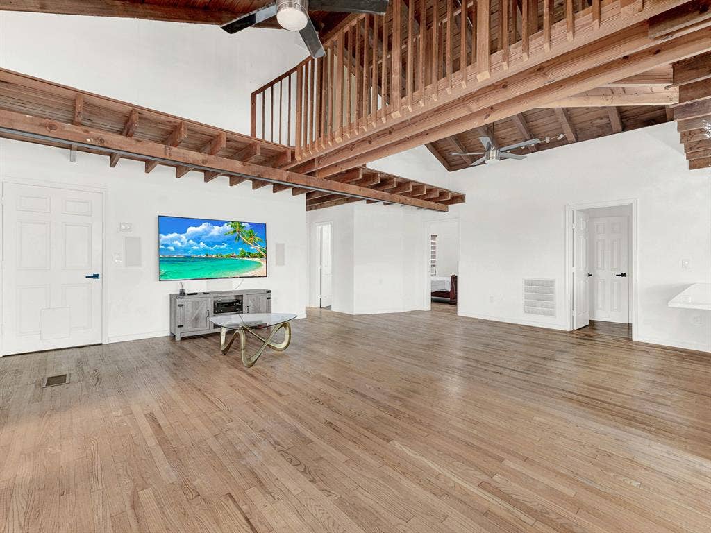 Open-concept interior featuring vaulted ceilings, exposed wooden structural beams, wood-finish flooring, and an elevated interior wooden railed overlook